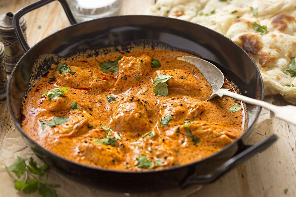 Golden chicken curry plated in a skillet with naan nearby