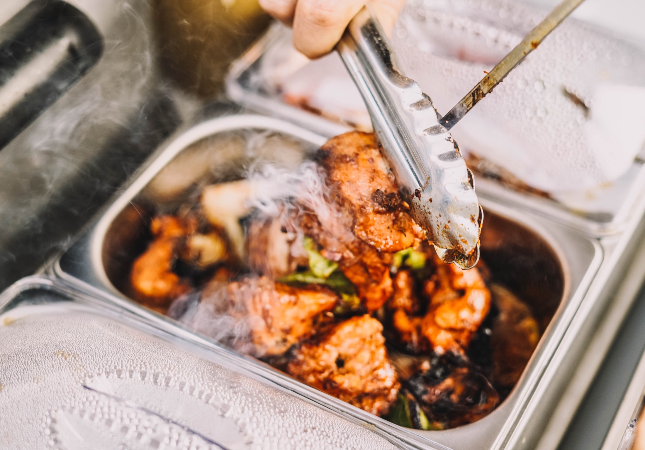 A hot catered dish being served with tongs