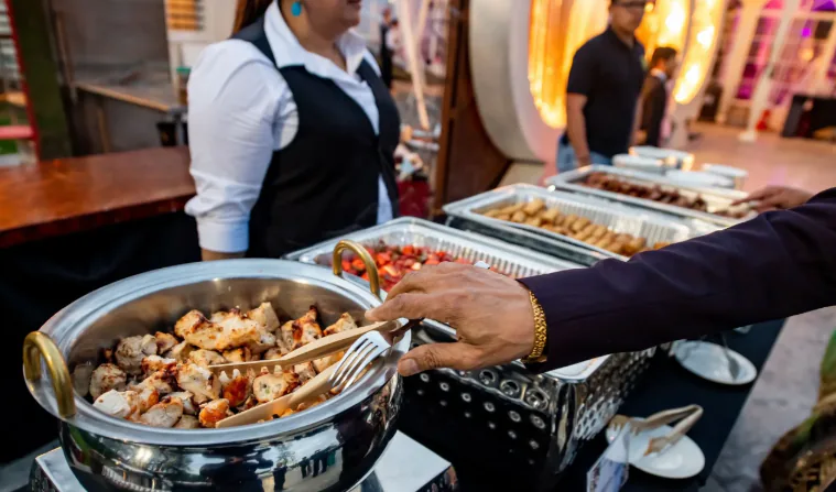 Outdoor catered buffet trays with guests and service staff nearby