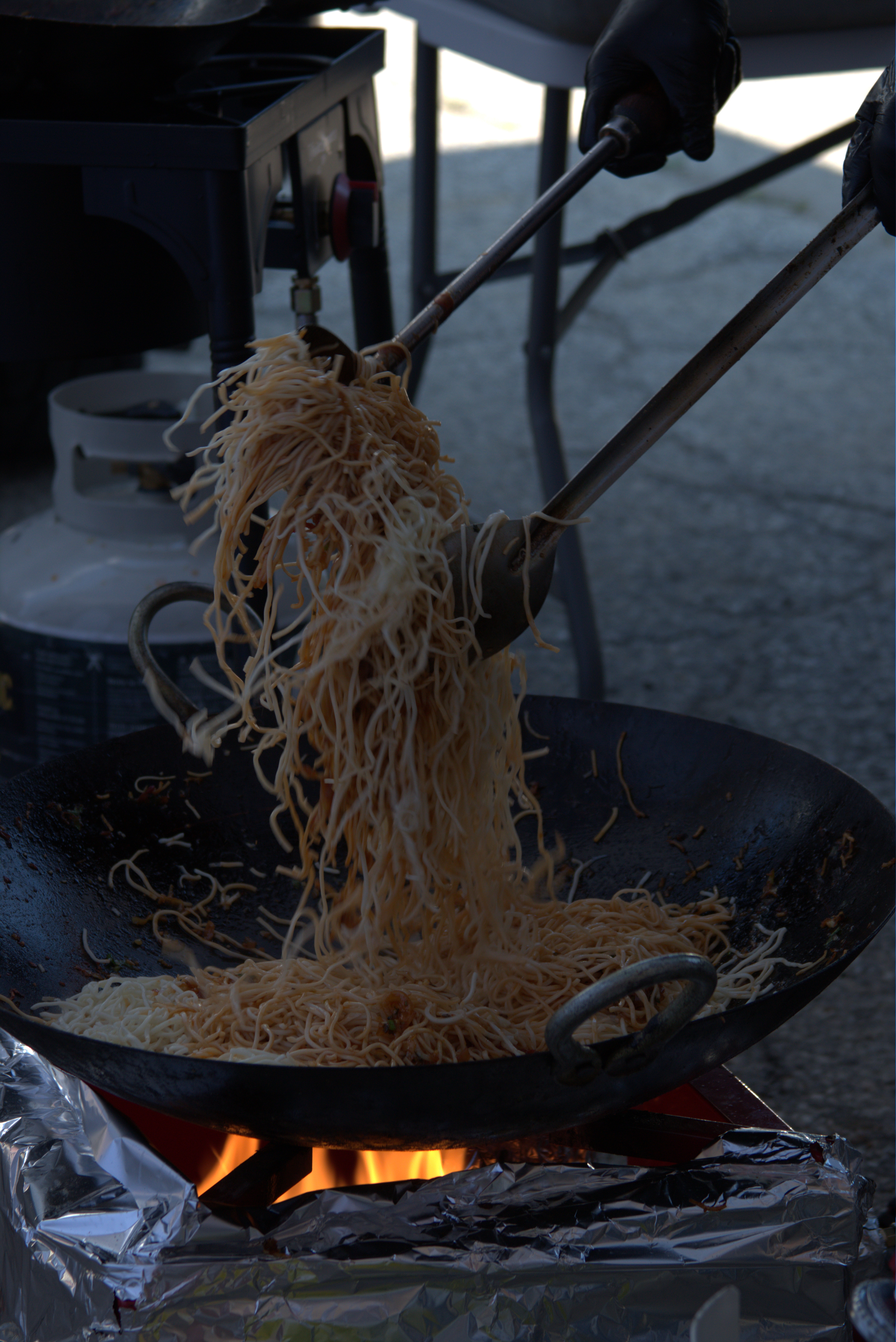 Fresh noodles being tossed at a live outdoor catering station