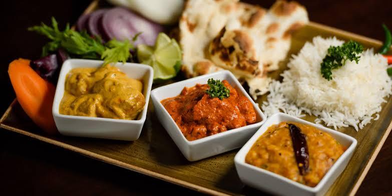 A plated Indian meal with naan, rice, and three small curries arranged for a daytime celebration