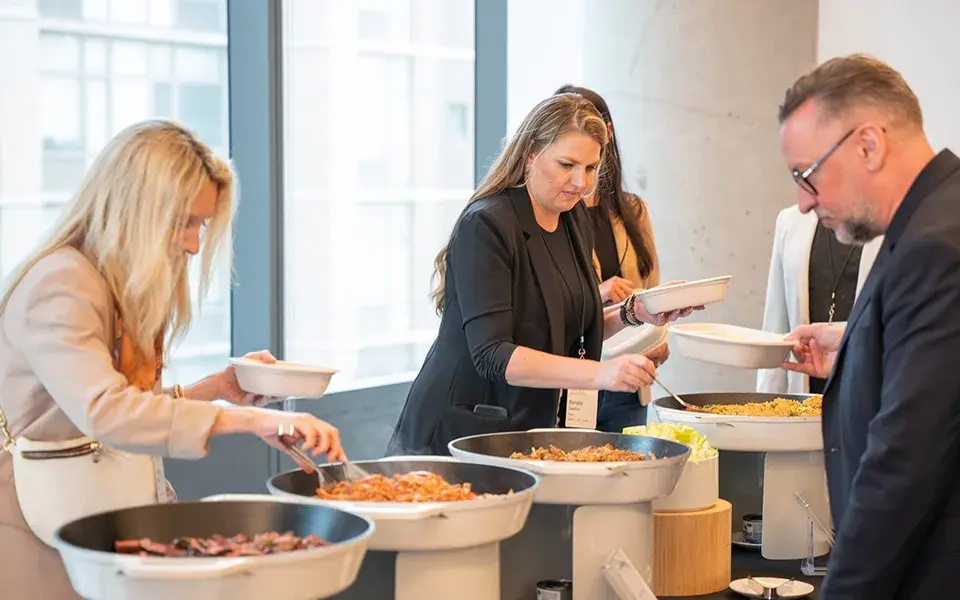 Guests building hot bowls from a corporate catering station set beside large windows