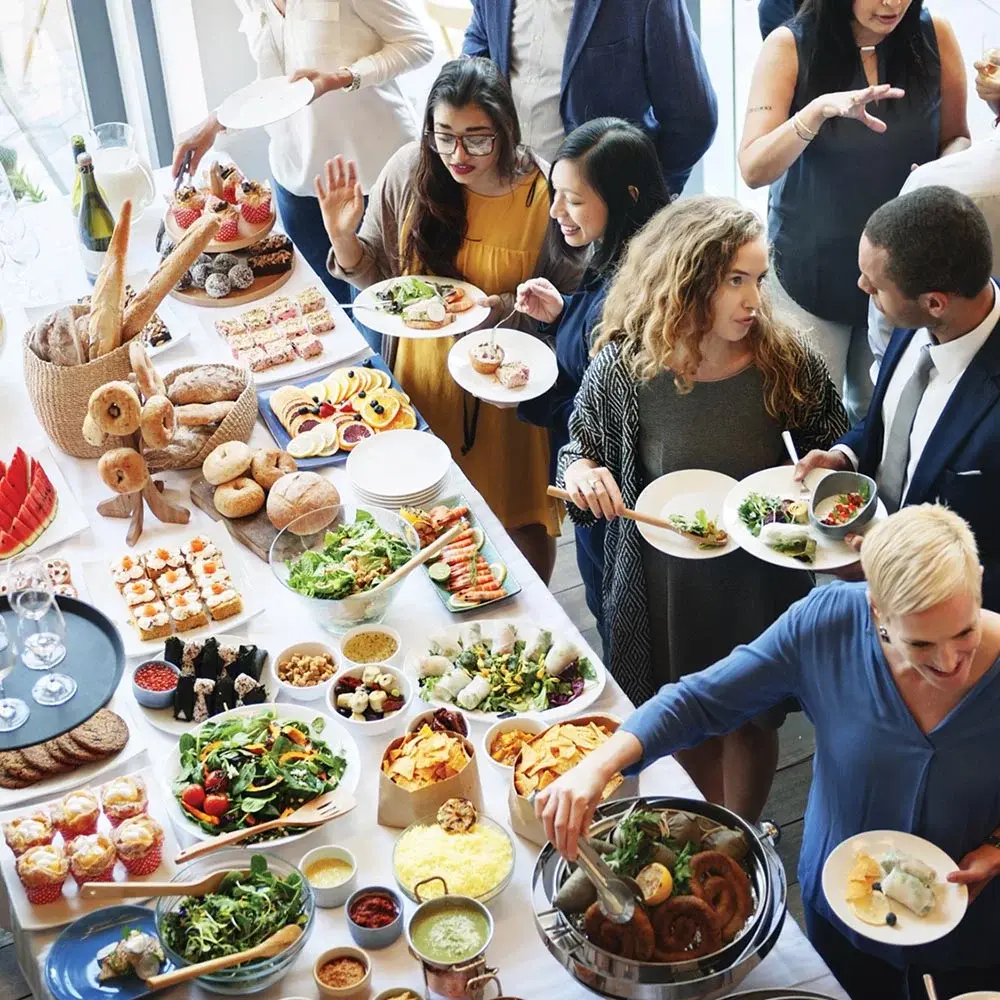 Guests gathering around a brunch-style corporate catering spread with pastries, salads, and plated bites