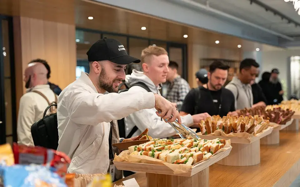 Conference guests moving through a corporate lunch line with stacked sandwiches and grab-and-go catering trays