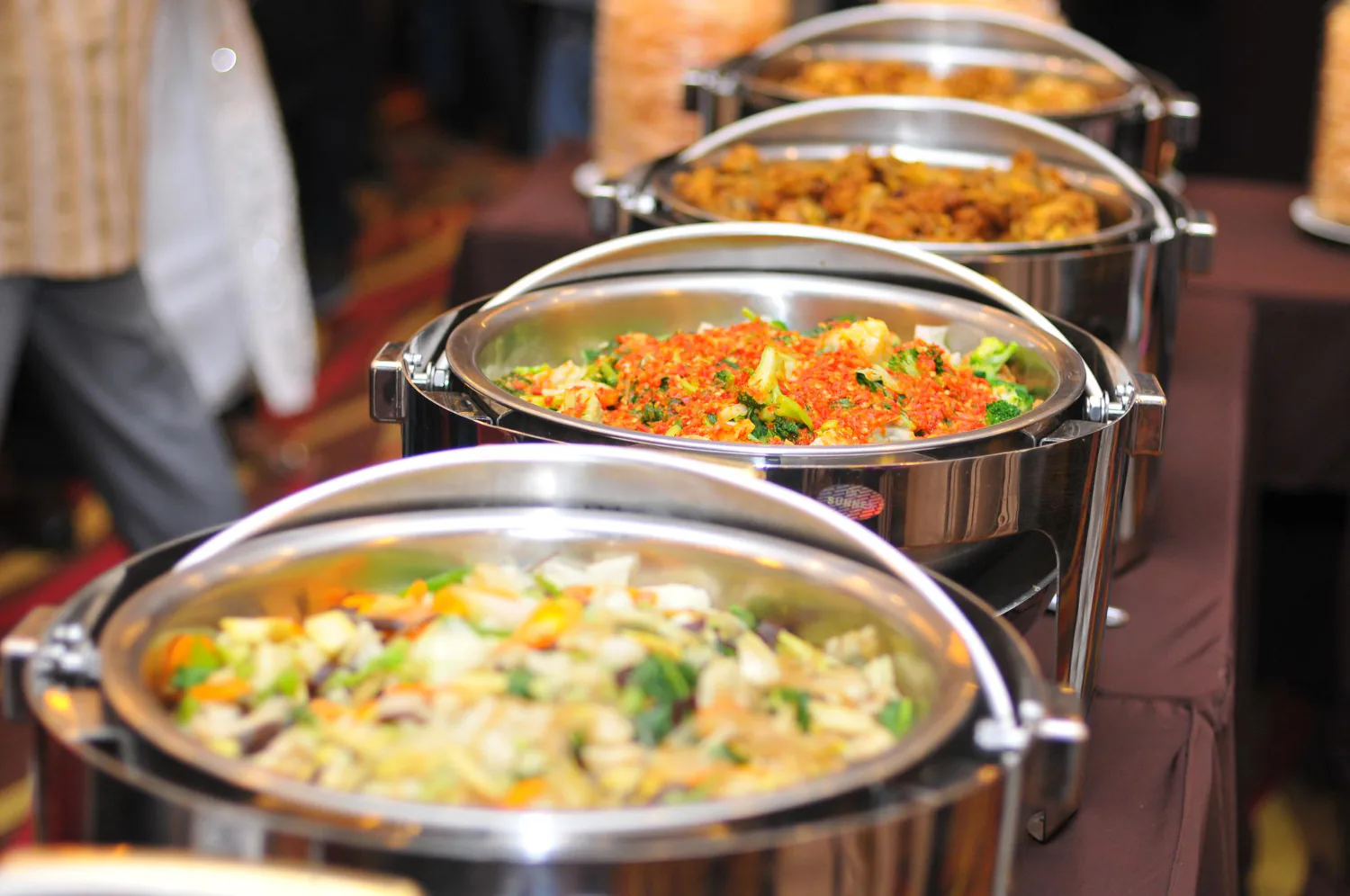 A line of hot chafers filled with vegetable dishes prepared for a community gathering
