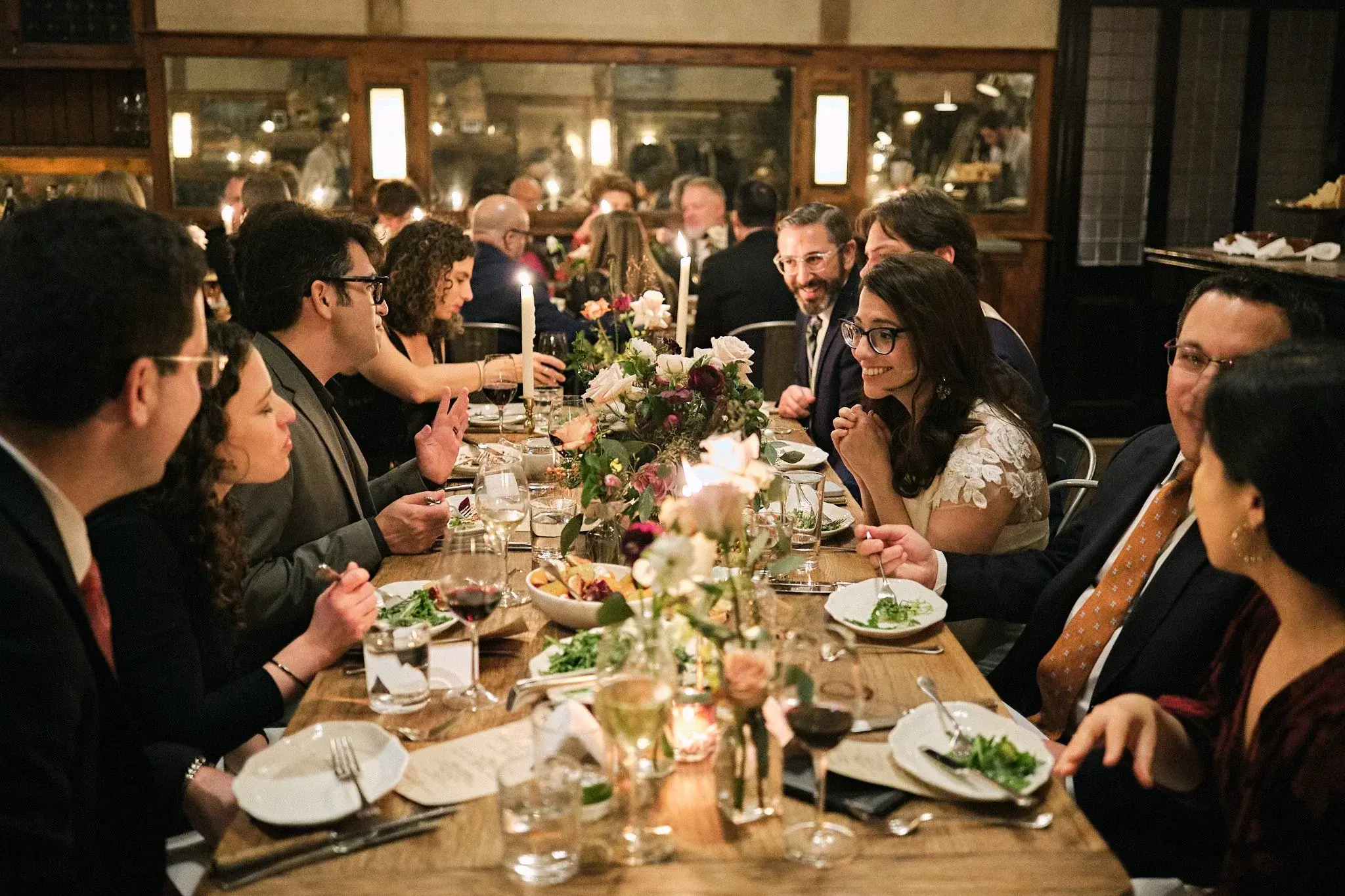 Guests gathered around a candlelit private-room dinner table with florals and plated courses during an engagement or anniversary celebration