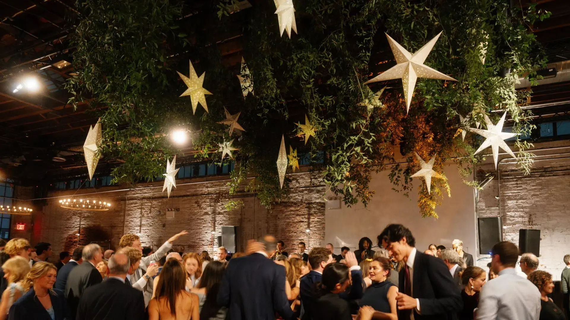 Guests celebrating beneath hanging greenery and illuminated star decor on a busy indoor dance floor