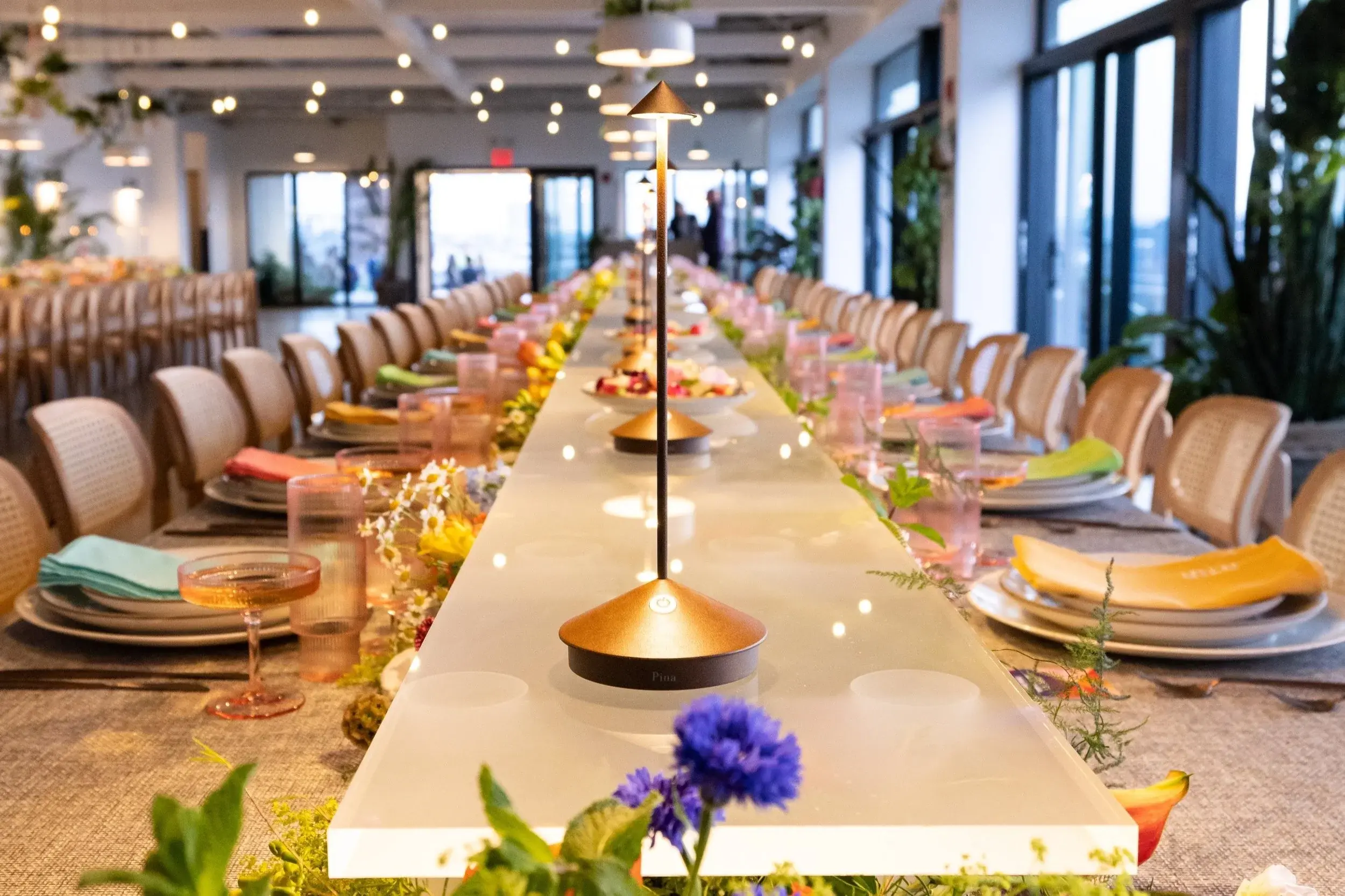 A long indoor banquet table styled with florals, colourful napkins, and place settings for a milestone dinner