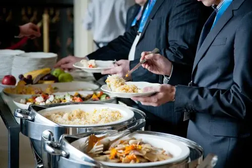 Guests in formal attire serving themselves from a memorial buffet line with chafers and plated sides