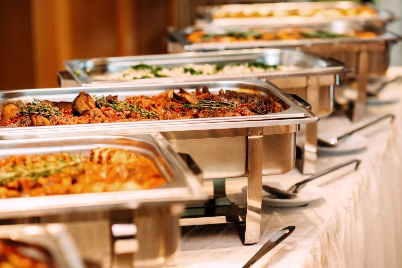 A line of polished chafer trays filled with hot entrees and rice prepared for memorial catering service