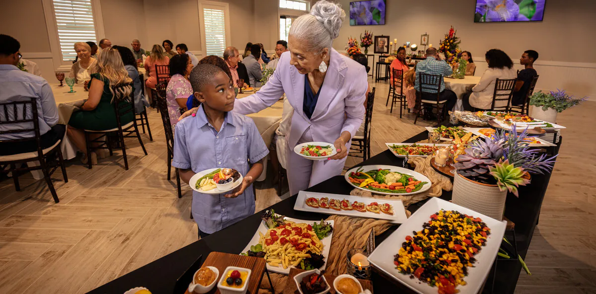 Family members gathering around plated food and buffet displays during a memorial meal in a reception room