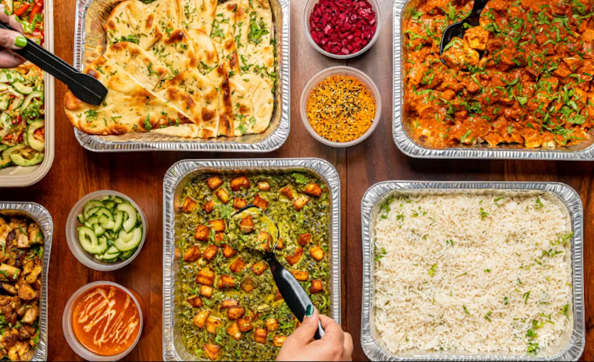 A top-down office lunch buffet with naan, rice, paneer, curry trays, and labelled sides arranged for team service