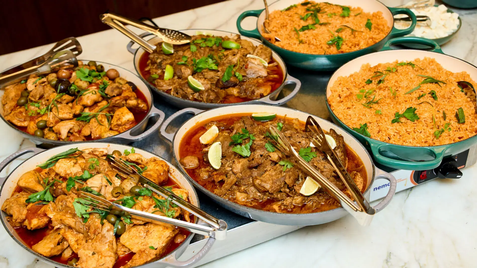 Large serving pans of braised entrees and rice set out for a generous office lunch buffet