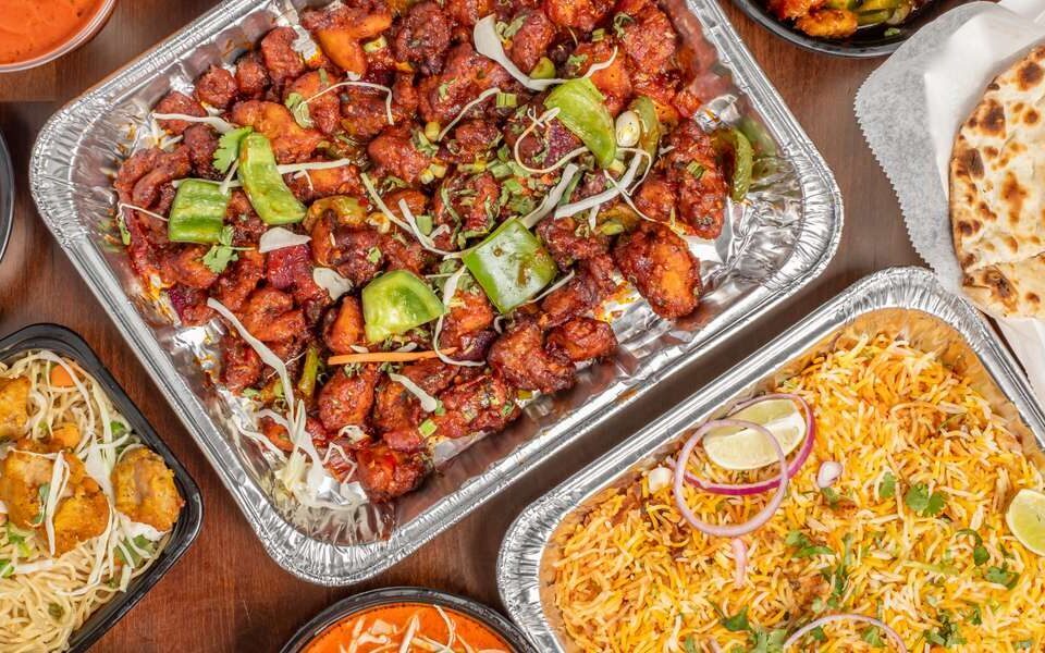 Hot office lunch trays filled with biryani, tandoori bites, and curry sides arranged for a workplace meal
