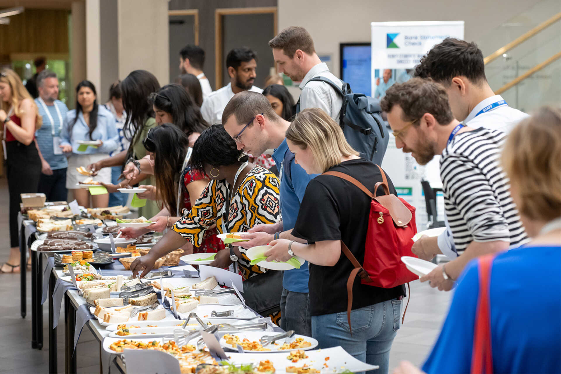 Guests lining up along a long lunch buffet with sandwiches, plated bites, and desserts during an education conference or campus program