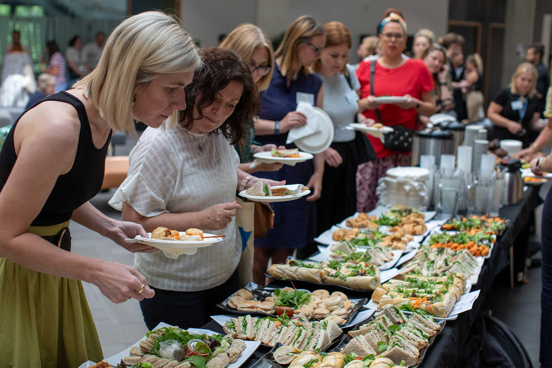 Attendees choosing sandwiches, salads, and coffee from a staffed pickup table during a school or campus gathering