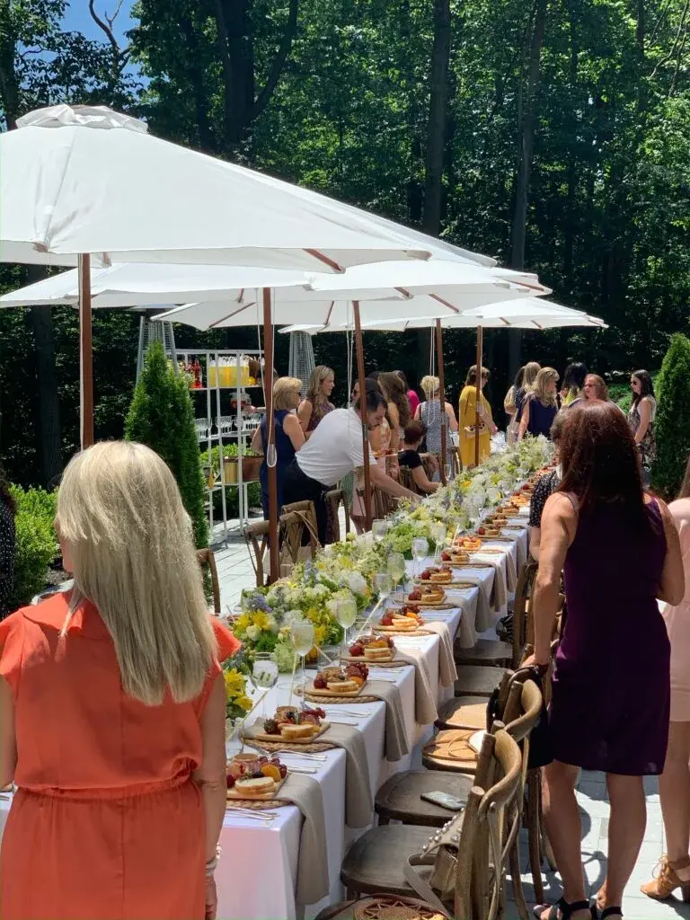 Guests mingling beside a parasol-lined brunch table arranged for a daytime private gathering