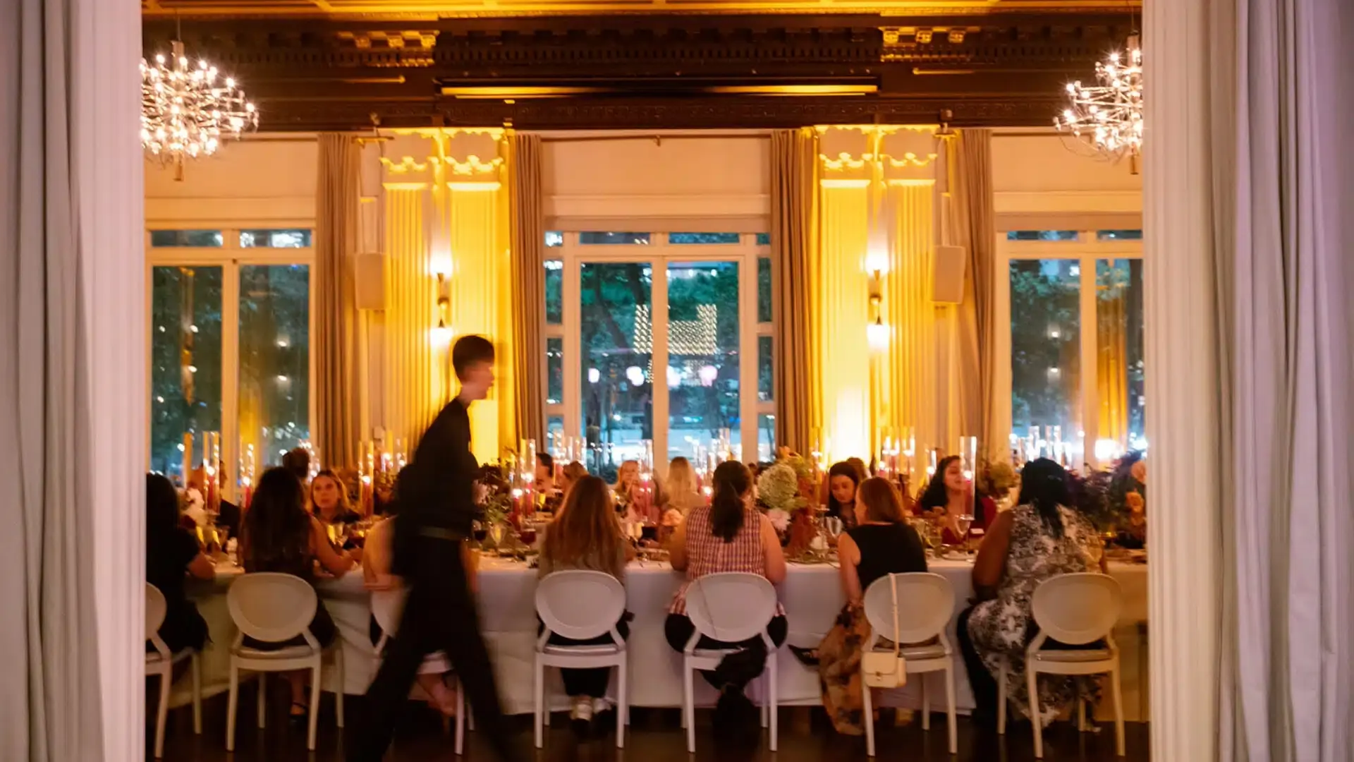 A candlelit indoor private dinner with guests seated around a long table in a warm dining room