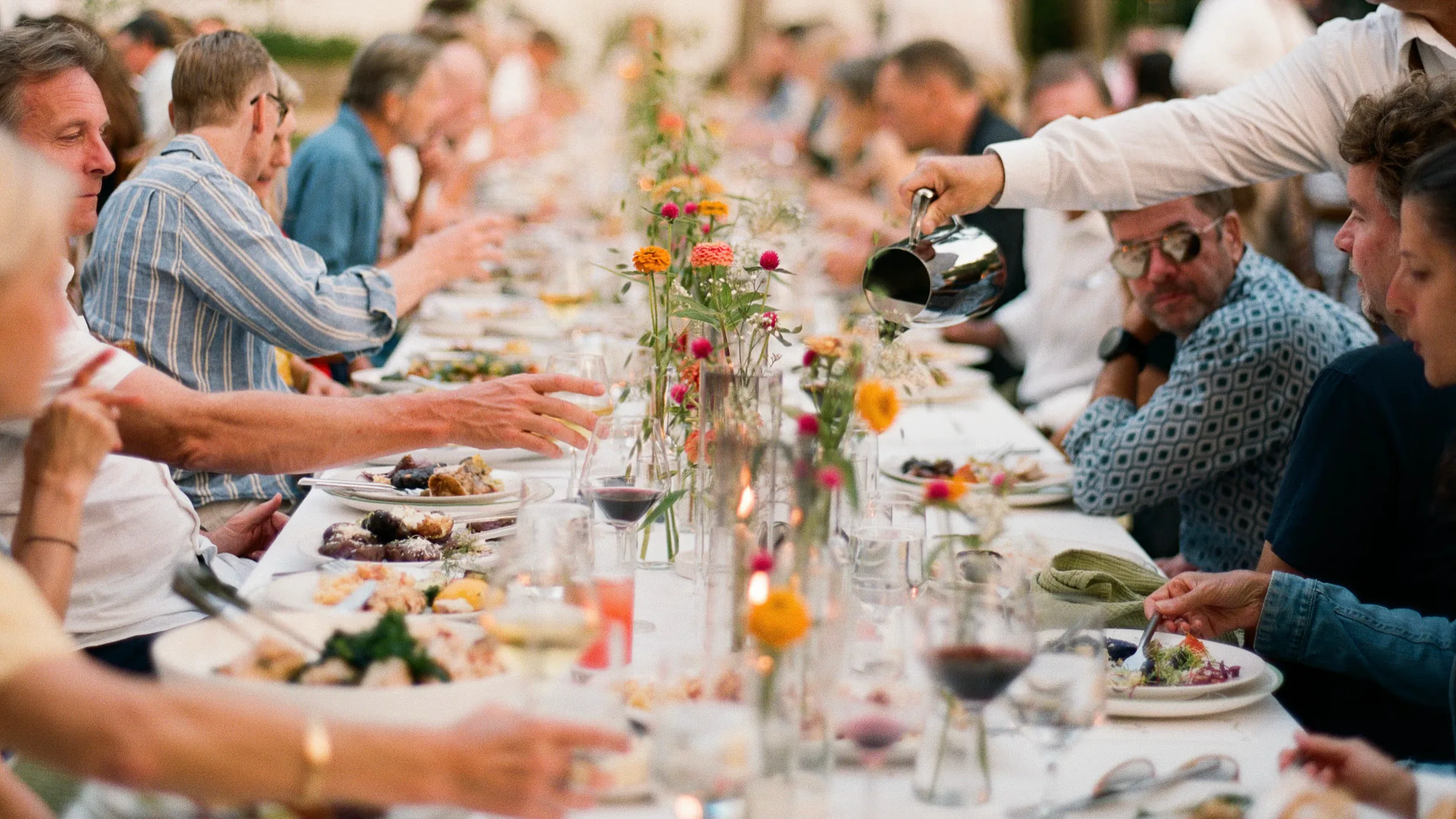 Guests dining together at a long candlelit table while servers pour drinks during an intimate private event